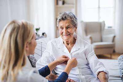 Pflegerin knöpft einer lächelnden Seniorin die Bluse zu Pflegerin knöpft einer lächelnden Seniorin die Bluse zu