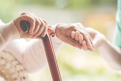 Eine helfende Hand stützt die Hand einer älteren Person am Gehstock Eine helfende Hand stützt die Hand einer älteren Person am Gehstock